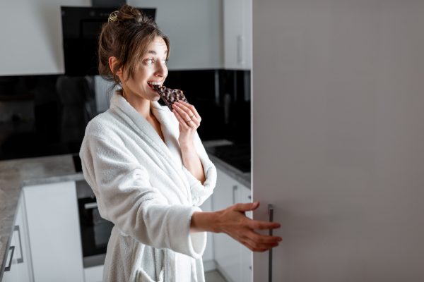 femme qui mange du chocolat en ouvrant son frigo