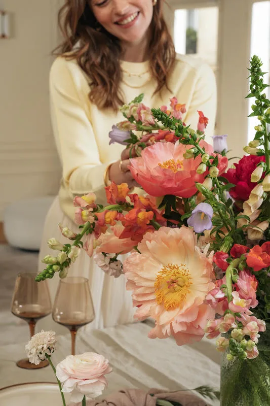 Femme à côté d'un beau bouquet de pivoines dans un vase