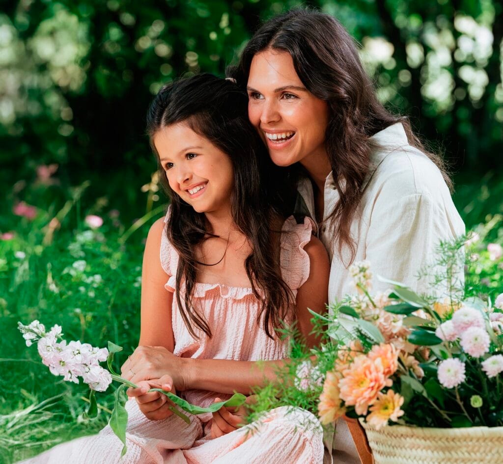 Une mère et sa fille souriantes, tenant des fleurs, assises dans l'herbe