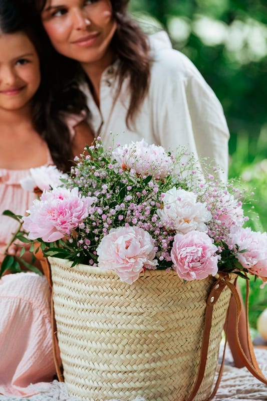 Une bouquet de fleurs dans un sac et en fond une maman et sa fille