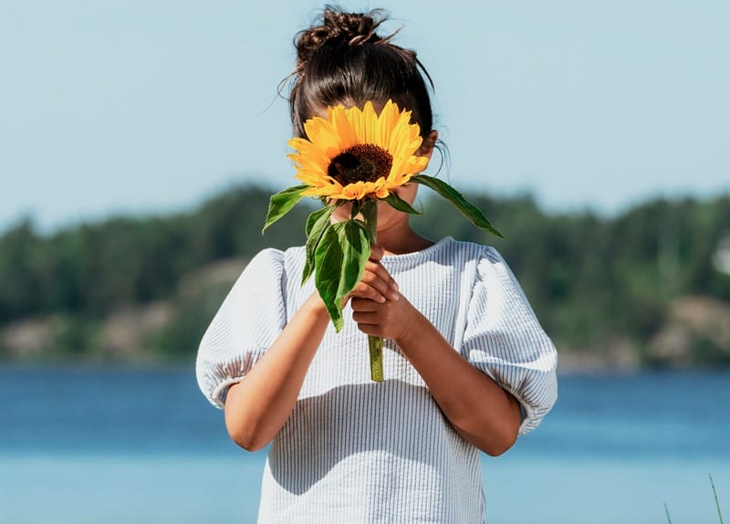 Petite fille tenant un tournesol devant son visage