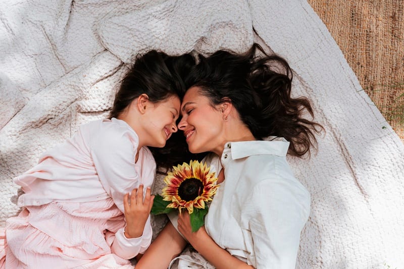 Une mère et sa fille allongées au sol tenant un tournesol