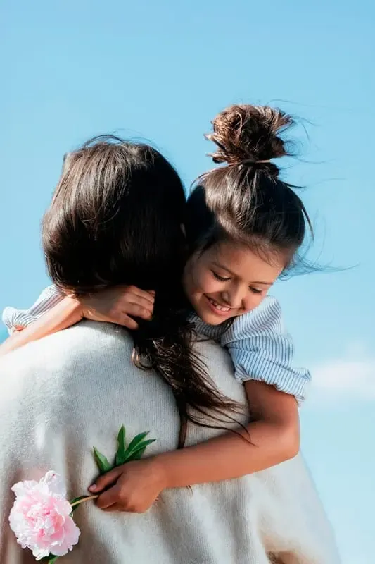 Une fille souriante, dans les bras de sa mère, tenant une pivoine