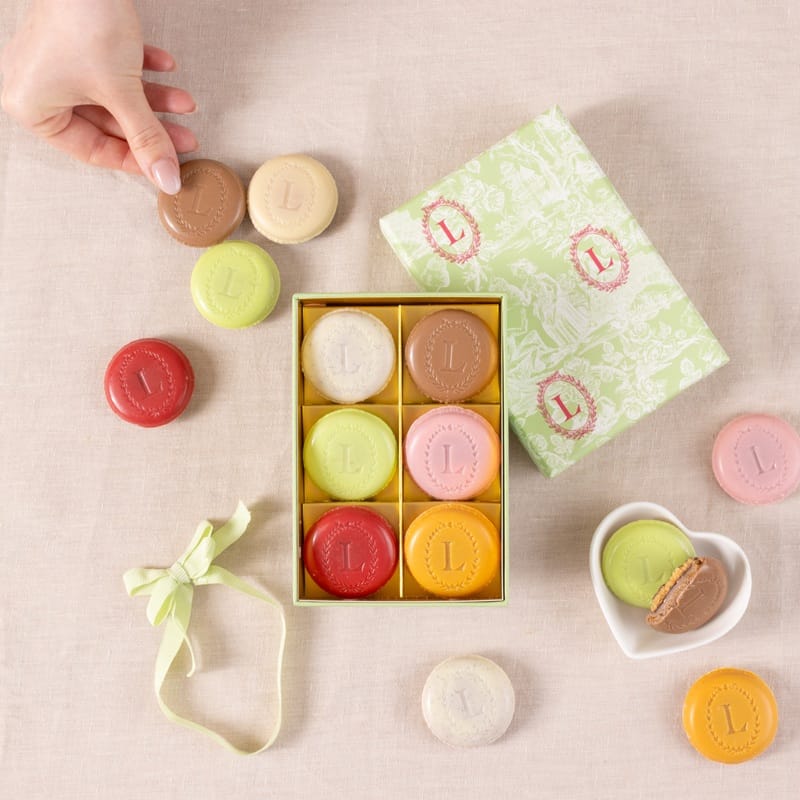 Boîte de macarons Ladurée ouverte, une main attrapant un macaron