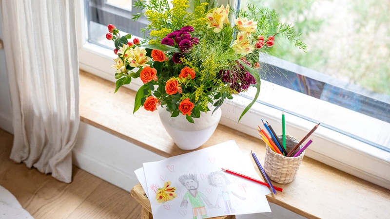 Un bouquet de fleurs et un dessin d'enfant posés sur le rebord d'une fenêtre