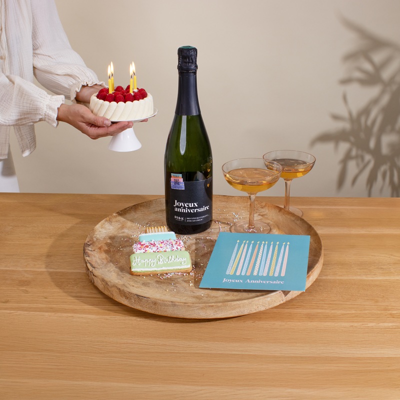 Bouteille de champagne, verres pour trinquer, carte joyeux anniversaire et bougies sur un gâteau disposés sur une table