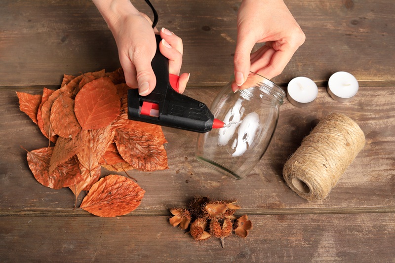 Personne collant des feuilles d'automne sur un bocal en verre pour créer une lanterne