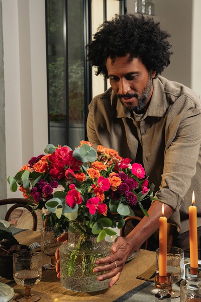 Homme décorant une table avec un bouquet de fleurs d'automne dans un vase