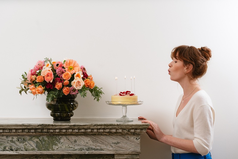 Femme soufflant des bougies sur un gâteau d'anniversaire, un bouquet de fleurs posé devant elle