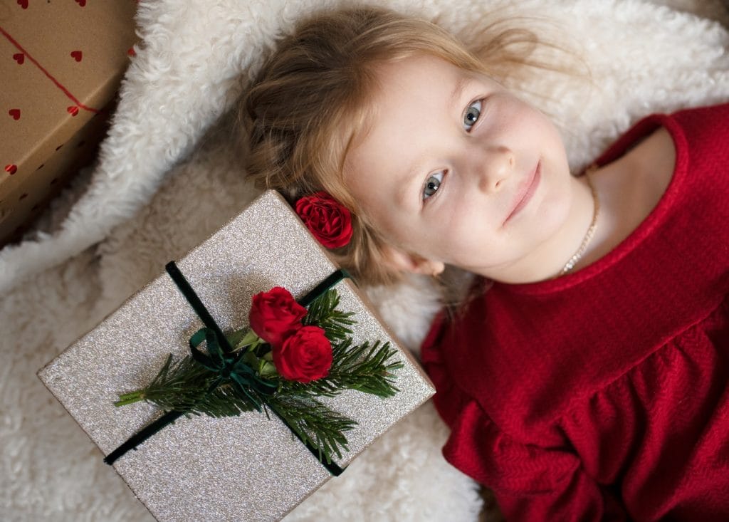 Petite fille qui sourit couchée à côté d'un cadeau de Noël à l'emballage blanc avec des roses