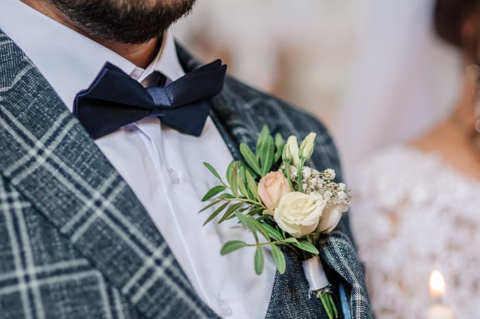 Un marié avec un costume à carreaux et une boutonnière de roses blanches et roses