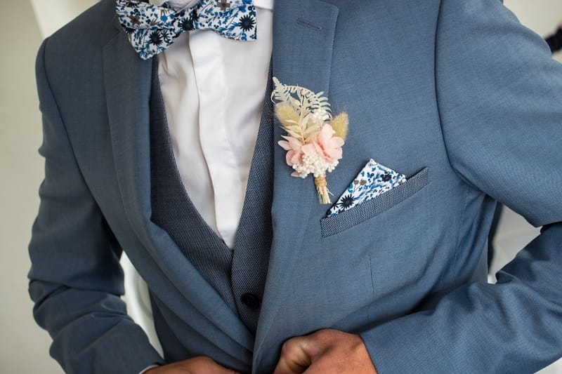 Un marié en costume bleu avec une boutonnière en fleurs rose pâle et crème