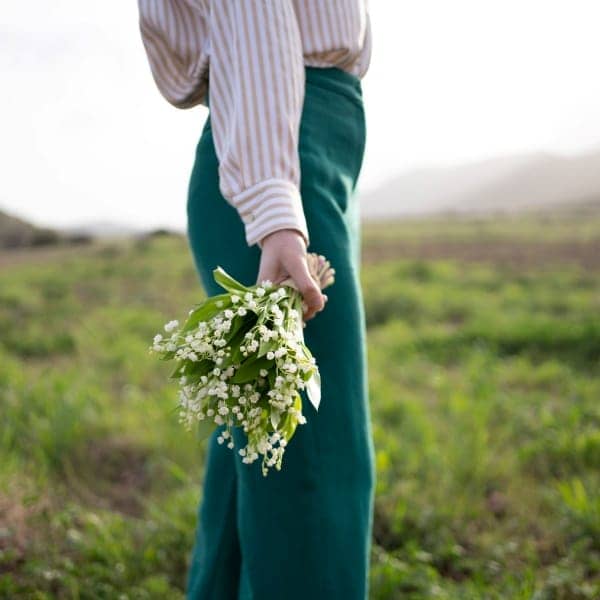 une femme tient un bouquet de muguet dans un champ