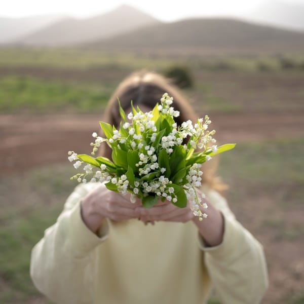 une femme tient un bouquet de muguet du 1er mai devant son visage