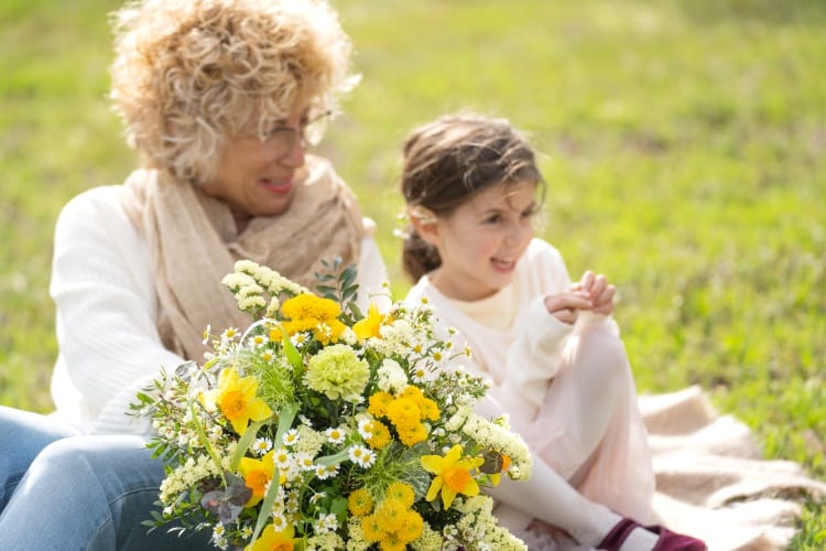 une grand-mère et sa petite-fille dans un parc avec un grand bouquet de fleurs