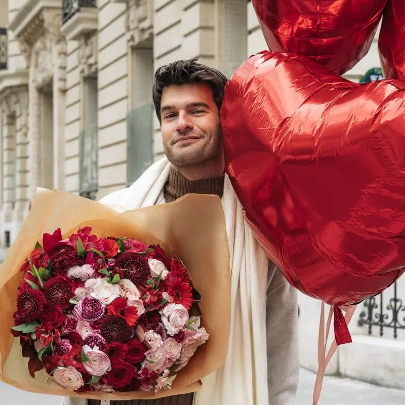 Homme avec un bouquet des fleurs rouges et des ballons rouges