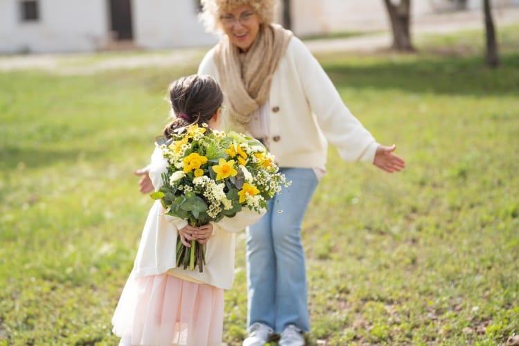 Une petite-fille tient un bouquet dans son dos pour l'offrir à sa grand-mère