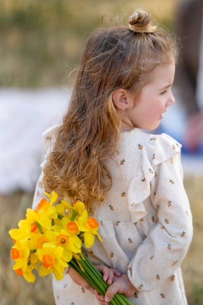 une petite-fille tient un bouquet de jonquilles dans son dos