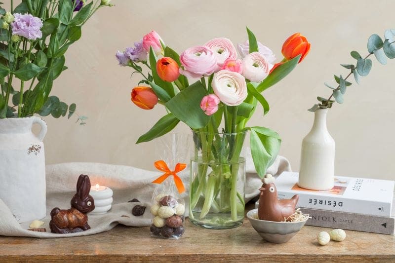 Table avec oeufs, poule et lapin en chocolat avec un bouquet de fleurs