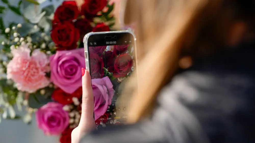Femme qui est en train de faire une photo à un bouquet de roses avec son téléphone